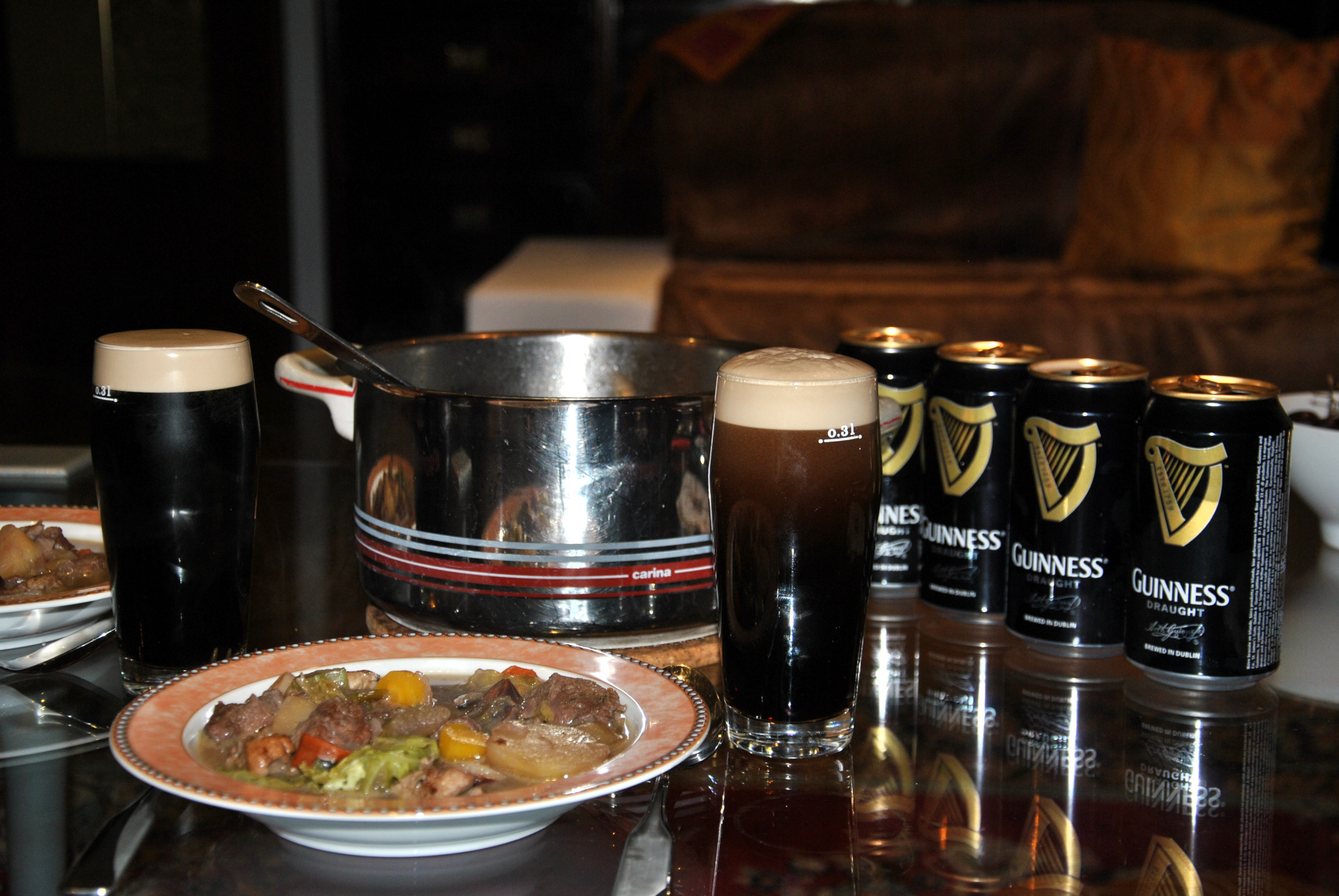 Ein Foto von einem Irish Stew und einem Glas Guinness mit Guinness Dosen im Hintergrund.
