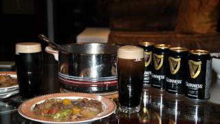 Ein Foto von einem Irish Stew und einem Glas Guinness mit Guinness Dosen im Hintergrund.